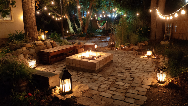 16 Cozy and Modern Backyard Fire Pit Ideas 6 Backyard fire pit surrounded by string lights and glowing lanterns at night.