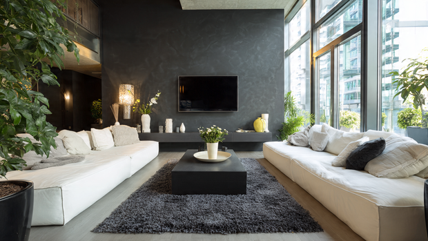 A sleek living room featuring a dark matte TV wall contrasted by light furniture and open space.